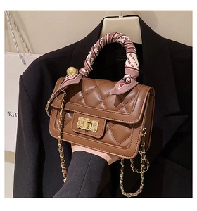 Detail of brown quilted crossbody bag featuring gold twist lock and scarf-wrapped handle