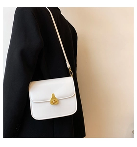 Minimalist white square crossbody bag featuring a golden teardrop twist lock on a black blazer