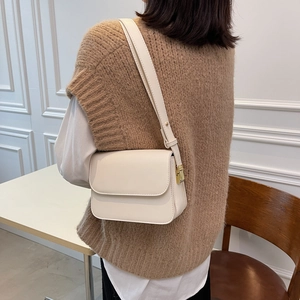 Detail of minimalist cream square shoulder bag featuring elegant gold hardware on side