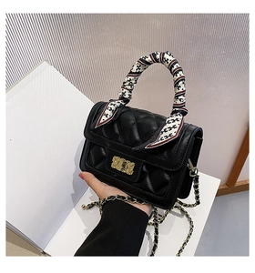 Detail of black quilted leather handbag with gold clasp and silk scarf handle