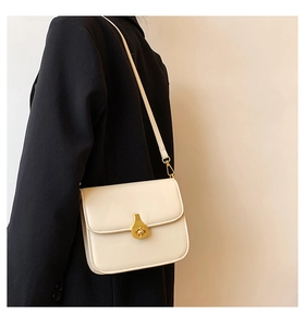 Detail of a creamy white rectangular crossbody bag with a gold teardrop lock on a blazer
