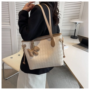 Detail of beige woven tote bag featuring brown leather trim and a cute puppy charm