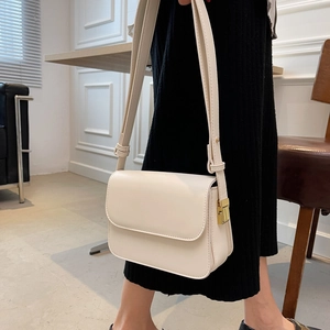 Detail of minimalist cream square crossbody bag with elegant gold metal flip lock clasp