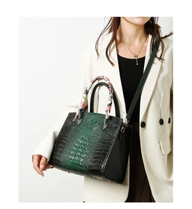 Detalle de bolso verde oscuro con textura de cocodrilo, pañuelo y tachuelas metálicas