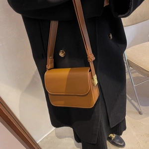 Close-up of minimalist brown leather crossbody bag with metal buckle on a black wool coat