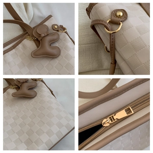Close-up of checkerboard texture, golden zipper, and bear charm on cream tote bag