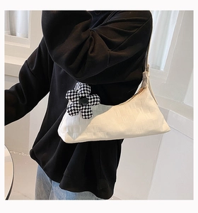 White underarm bag with textured fabric and checkered flower charm on black hoodie