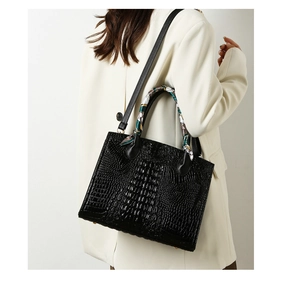 Detalle de bolso negro con textura de cocodrilo y pañuelo de seda decorativo en el asa