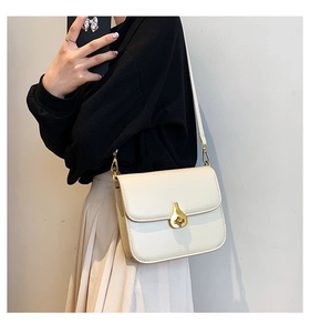 Detail of cream leather crossbody bag featuring a unique gold teardrop twist-lock closure
