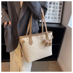 Detail of cream woven tote bag featuring dark brown handles and cute puppy charm accessory