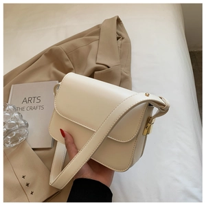 Detail of minimalist beige leather crossbody bag with elegant gold buckle on a blazer