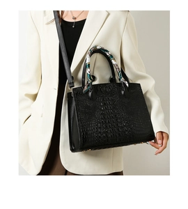 Detalle de bolso negro con textura de cocodrilo y elegante pañuelo de seda en el asa