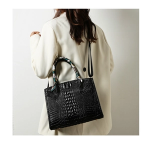 Detalle de bolso negro con textura de cocodrilo, pañuelo de seda decorativo y correa de hombro