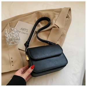 Close-up of black leather square bag with gold metal clasp on a beige blazer background