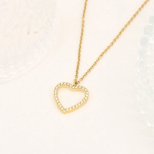 Dettaglio della collana a cuore dorata con pavé di zirconi su una superficie beige