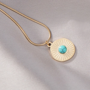 Detail einer goldenen Schlangenkette mit Sonnenanhänger und Türkis auf Seide