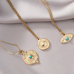 Detail von drei goldenen Evil Eye-Halsketten mit Türkis auf grauem Seidenhintergrund