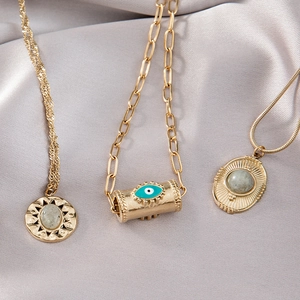 Trois colliers dorés avec pendentifs œil maléfique turquoise et disque solaire sur satin