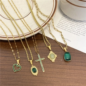 Série de colliers dorés avec pierres vertes, pendentifs croix et cœur sur fond de bois