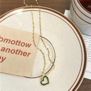 Collier cœur doré avec cristaux verts et chaîne fine sur une assiette minimaliste chic