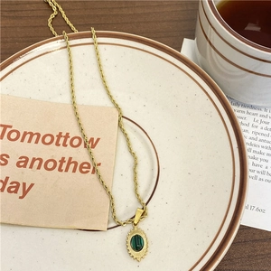 Collier chaîne torsadée dorée avec pendentif en malachite verte sur une assiette blanche