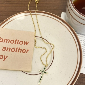 Collier croix doré vintage avec zircons verts sur une assiette en céramique