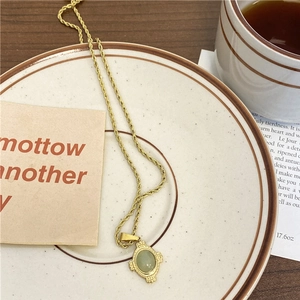 Détail d'une chaîne corde dorée vintage avec pendentif ovale en pierre verte sur une assiette