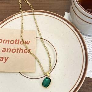 Gros plan du pendentif en pierre vert émeraude sur un collier en maille trombone dorée