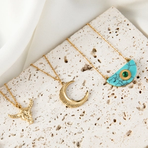 Golden necklaces with turquoise heart and celestial pendants on a neutral stone display