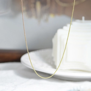 Gros plan d'un collier chaîne à billes dorées polies sur une assiette en céramique blanche