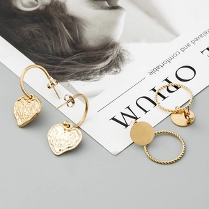 Elegant gold twisted hoop and hammered heart earrings displayed on a fashion magazine