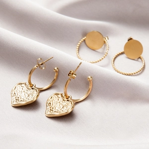 Detail of gold twisted hoop earrings and hammered heart drops on soft grey silk