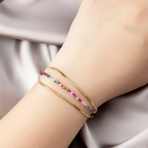 Three-layer bohemian beaded bracelet with gold chain on grey silk background