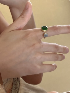 Close-up of gold open ring with emerald green and grey stones on a hand