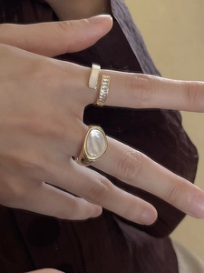Detailed view of two gold rings featuring white shell inlay and sparkling crystals on hand