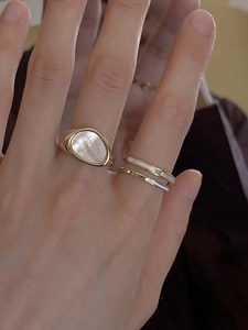 Detail of gold stacking rings featuring a white shell stone and Queen engraving