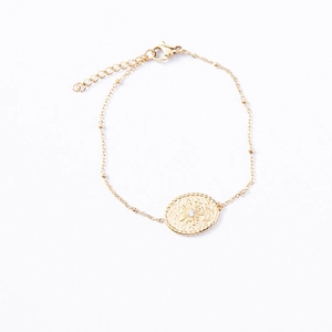 Détail du bracelet doré avec médaille ovale soleil et pierre en zircone cubique brillante