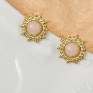 Boucles d'oreilles soleil dorées avec pierre rose naturelle sur plateau décoratif