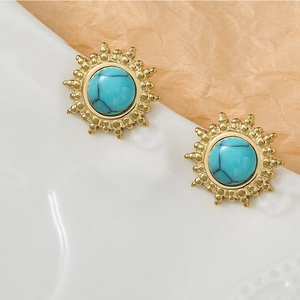 Boucles d'oreilles soleil bohèmes dorées avec pierre turquoise sur plat céramique