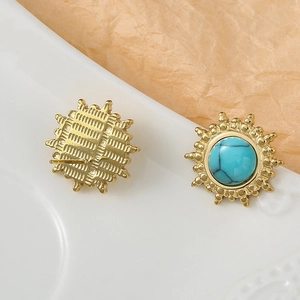 Détail de boucles d'oreilles soleil dorées avec pierre turquoise sur plateau céramique