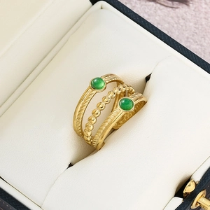 Detailed close-up of layered gold ring with green natural stones on leather display