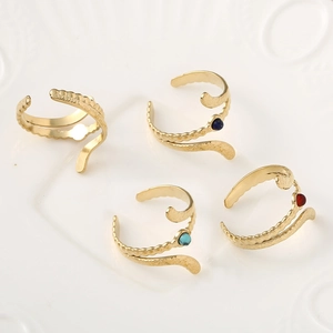 Adjustable gold snake wave rings set with colorful gemstones on a vintage ceramic plate