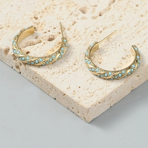 Golden twisted rope hoop earrings with blue turquoise stones on a stone display