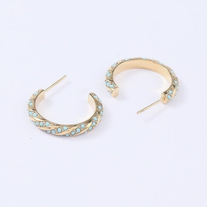 Detailed macro view of gold C-shaped hoop earrings with turquoise bead inlay accents
