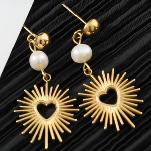 Detail of hollow heart earrings with sunburst texture and pearl accents on black fabric