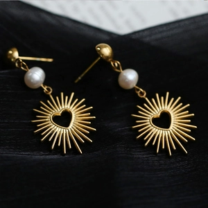Elegant gold drop earrings with white pearls and sunburst heart pendants on black fabric