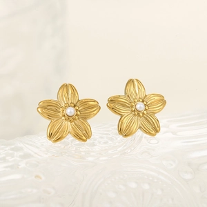 Boucles d'oreilles fleurs dorées avec pétales brossés et perles sur plateau verre