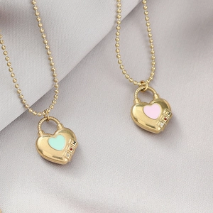 Collane con medaglione a cuore dorato e smalto rosa e menta su sfondo in tessuto morbido