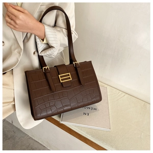 Detail view of large brown crocodile embossed tote bag with elegant gold metal buckle