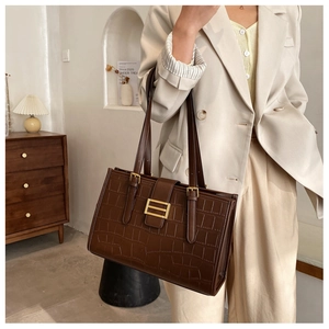Detail of dark brown faux leather bag with crocodile texture and gold metal buckle